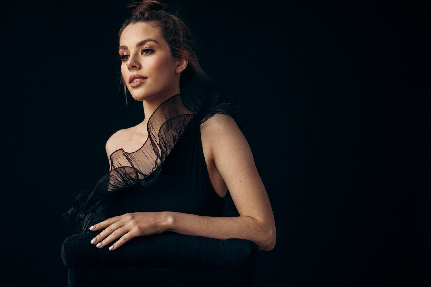 Woman in elegant black outfit against dark background.